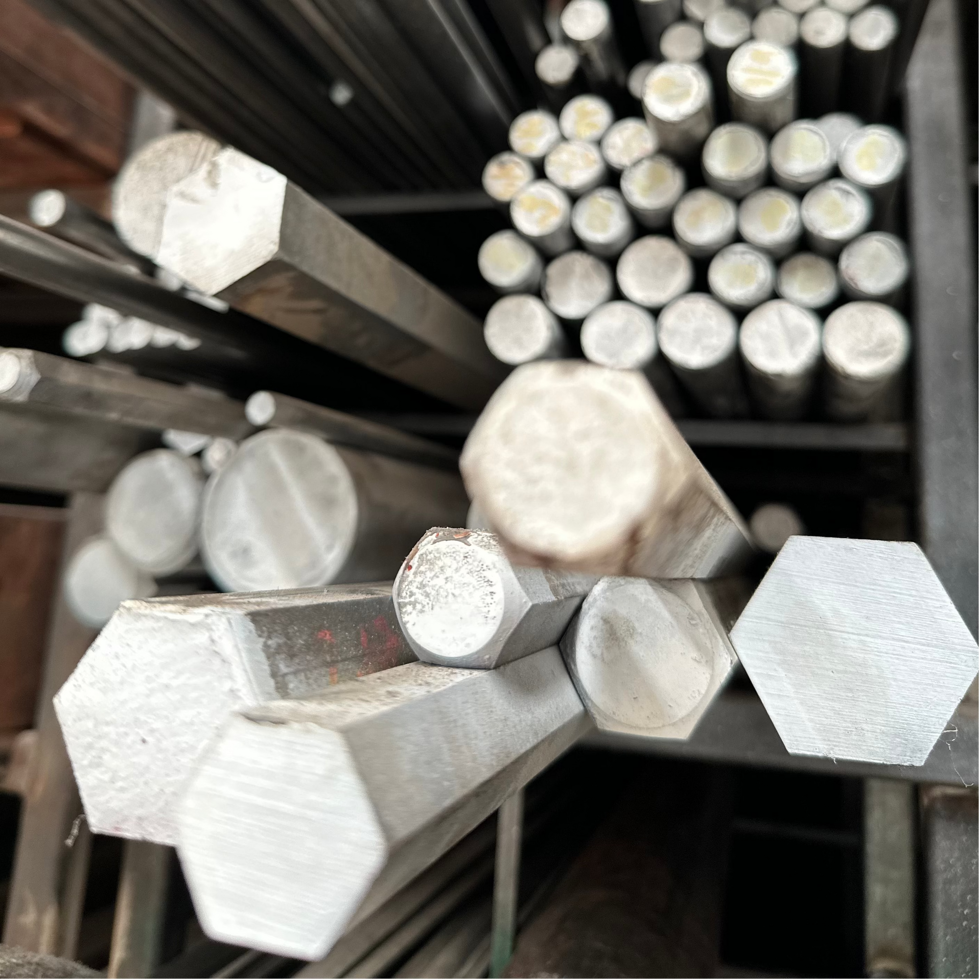 Fotografía de perfiles hexagonales de acero inoxidable en rack. Atrás se observan barras de inoxidable en rack.